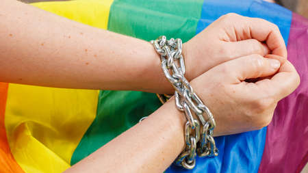 Female hands chained against the background of the LGBT flag. The concept of oppression an...