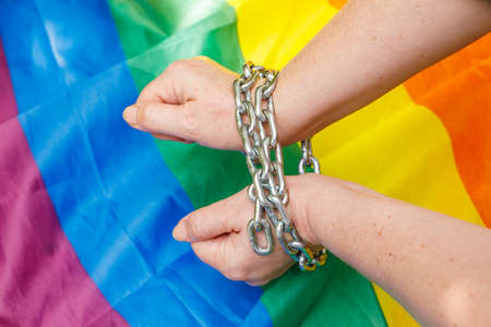 Female hands chained against the background of the LGBT flag. The concept of oppression an intolerance towards sexual minoritiesの写真素材