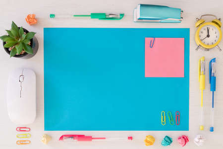 A large, blank blue card on the desk and a small pink card with space for text. Office accessories, alarm clock, computer keyboard, pens, crumpled paper balls, staples. Conceptの写真素材