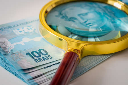 A bundle of Brazilian money with a magnifying glass on it, one hundred Reais banknotes, the highest denomination. Brazil currency fluctuation conceptの写真素材