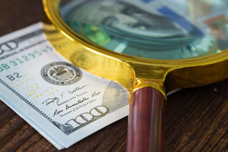 A bundle of USA money with a magnifying glass on it, one hundred dollars banknotes, the highest denomination. America currency fluctuation conceptの写真素材