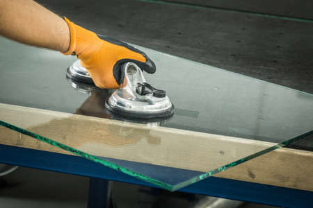 The Glazier uses a sucker for windows. Glass making workshop, The man lifts the pane of thick glass on the table with the help of specialized toolsの写真素材