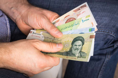 a man holding a bundle of Iranian money, Riyal, of varying valueの写真素材
