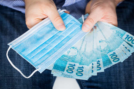 a man with outstretched hands, Brazilian money, lots and an anti-virus mask. The concept of the economic costs of a pandemic in Brazilの写真素材