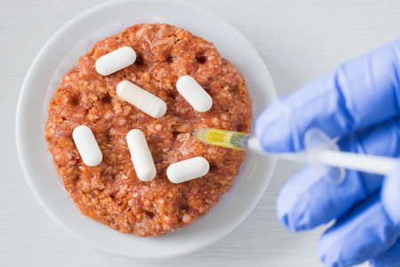 Raw Beef, Antibiotic Stuffing Food Concept. Hand in a lab technician sticking a syringe into meat