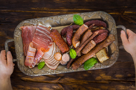Various types of appetizing cold cuts on a stylish tray. Background, old wooden table