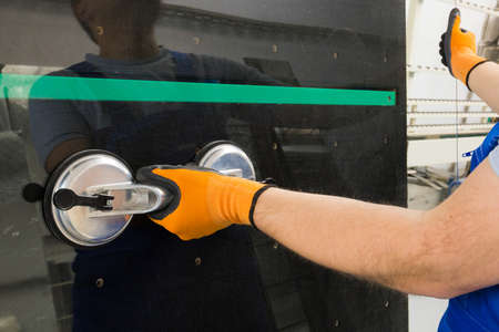 The glazier grasps the glass with a special suction cup on a professional table in the workplaceの写真素材