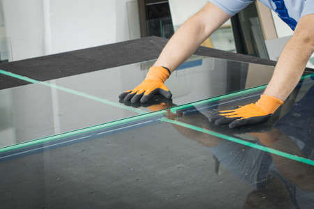 A worker cuts and breaks glass on a professional table in a workplaceの写真素材