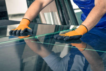 A worker cuts and breaks glass on a professional table in a workplaceの写真素材