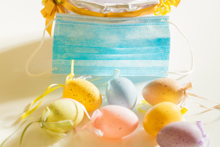 Easter eggs lying on the table with a mask to protect against coronavirus. The concept of holidays in the face of the third wave of the virusの写真素材