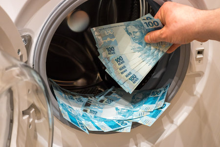 Brazilian money, the concept of money laundering from illegal activities. The man puts a large amount of banknotes into the washing machineの写真素材