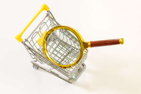 A miniature shopping cart with a magnifying glass. Economic and business concept, rising inflation and economic upheaval, white backgroundの写真素材