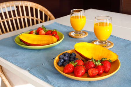 a healthy meal, two plates of fresh strawberries, mangoes, and blueberries, and orange juice on the...