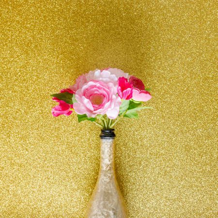 bouquet of flowers in a bottle of champagne. shiny gold background, creative, minimal party composition, celebration layoutの写真素材