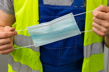 Manual worker holding an anti-viral mask, Workplace protection conceptの写真素材