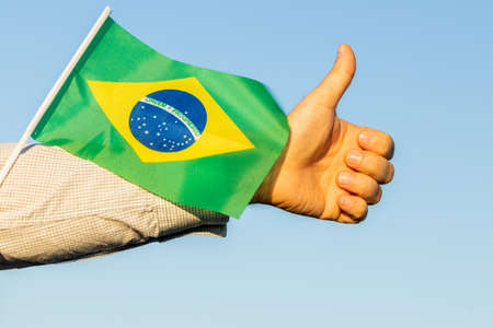 A man holding a flag of brazil in his hand and holding his thumb up in a gesture of joy and satisfactionの写真素材