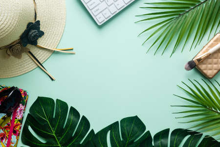 Flat creative frame of tropical nature, palm and Monstera leaves on a pistchio background with laptop, feminine hat, notebook, sunglasses, digital nomad and life balance concepts.の写真素材