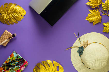 Flat creative frame of tropical nature, abstract colors, golden leaves on a purple background, laptop, feminine hat with colorful notebook and sunglasses, Concept, digital nomad, balance of work and life.の写真素材