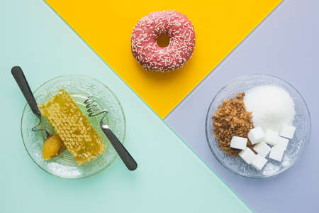 Healthy and unhealthy sugar, Three Colorful background with sweet products, Plate with various types of sweeteners and a donut as processed sugars and a golden honeycomb of natural honey, Health symbolの写真素材