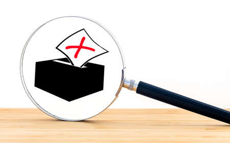 A magnifying glass in the background of a picture with a voting box and a marked ballot paper,...