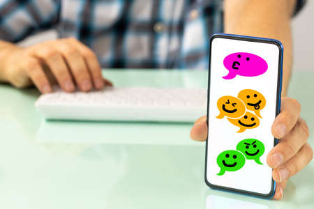 The man behind the desk shows the phone with comic speech bubbles of people talking via social messengers, Hand-drawn happy faces,の写真素材