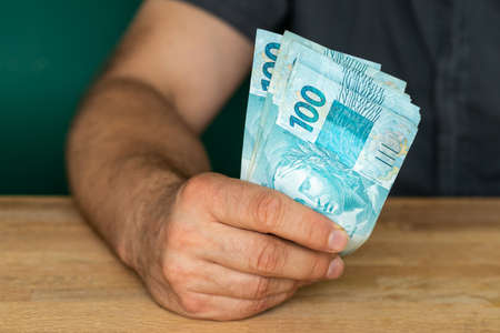 Brazilian money, Business success, lottery win Creative financial concept, A man in a shirt holds money spread out in his hands, File of banknotes of 100 reaisの写真素材