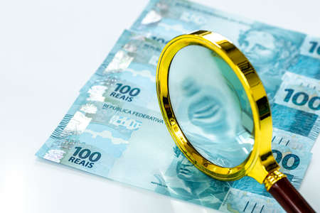 Brazil money, flat lay, 100 reais banknotes, magnifying glass, white background, business and financial concept, market and inflation observation, currency stabilityの写真素材