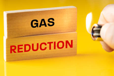 Gas reduction, written on a wooden block, yellow background, a burning lighter in hand, the concept...