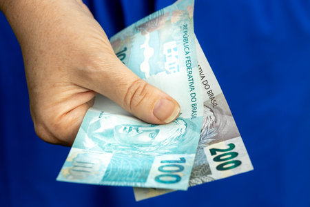 Brazilian money, Woman in a blue dress, Holding banknotes in hand, one hundred and two hundred Reais, Highest denominations, Financial conceptの写真素材