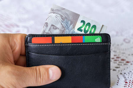 A wallet with a credit card and a Brazilian 200 Reais banknote in hand