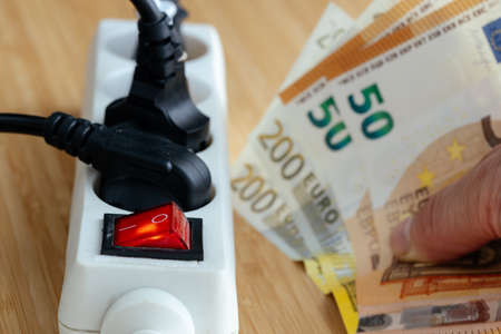 Increases in electricity prices in the European Union, Energy concept, Power strip with plugs connected and a large euro file in hand, Increase in energy prices for households and industry in Europeの写真素材