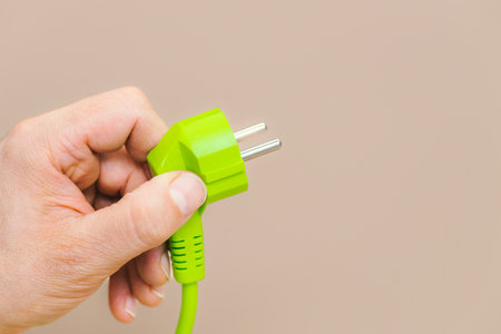 Green plug in hand, Latte-colored background, The concept of using green energy and the use of modern methods of obtaining energy in harmony with the natural environmentの写真素材