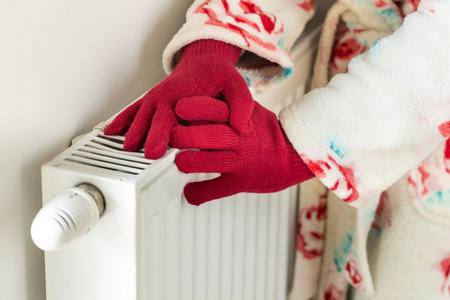 House and apartment heating costs. Rising energy prices, A woman with woolen gloves touches a cold radiator, Fears of winter and cold, power and gas outagesの写真素材