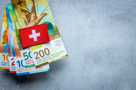 Swiss flag lying on a stack of Swiss francs, Currency of Switzerland, business and finance concept, copy space, gray backgroundの写真素材
