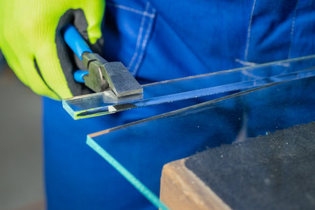 A glazier breaks off a small piece of thick glass by hand using a specialized breaker, Works in a glass factory, close upの写真素材