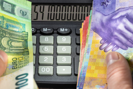 Currency rates, euro and Swiss franc pair, Financial concept, hands full of money, One hand full of euro banknotes, the other with Swiss currency, big calculator inside, Currency exchange rateの写真素材