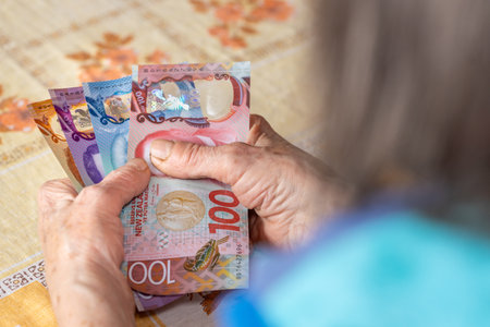 Household budget of older people in New Zealand. Economic concept, Pensioner woman holds several 50, 10 and 100 dollar banknotes in her hands, Financial situation of elderly peopleの写真素材