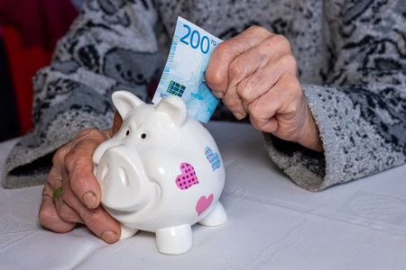an old lady puts 200 norwegian kroner into a piggy bank. financial concept