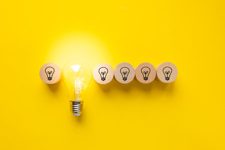Glowing light bulb and light bulb icons on round wooden blocks. Beautiful yellow background. Concept of ingenuity, technological development, Future ideaの写真素材