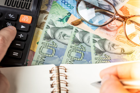 Costa Rica money, financial analysis, company accounting, tax calculation, financial business concept. Costa Rican colones together with a calculator, hand writing down the results in a notebookの写真素材