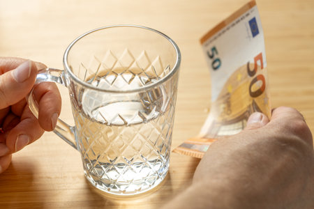 A glass of water and a 50-euro bill in hand. Economic concept. Rising water prices. Freshwater...
