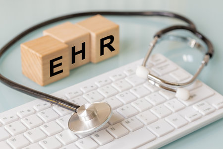 EHR, Electronic Health Record, written on wooden blocks. Doctor's office, Stethoscope and computer...