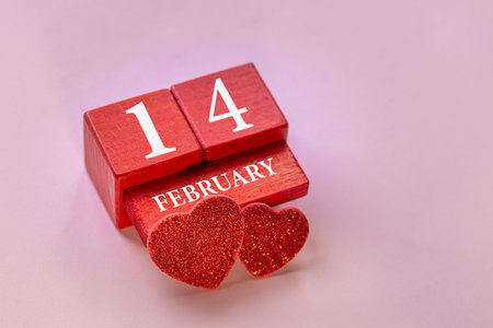 Valentine's Day composition with a wooden calendar and two red hearts on a pink background. Copy...