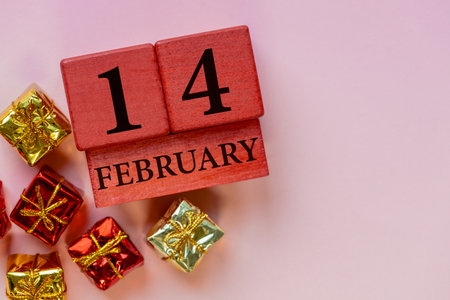 February 14. Valentine's Day composition with a wooden calendar and gift boxes on a pink background....