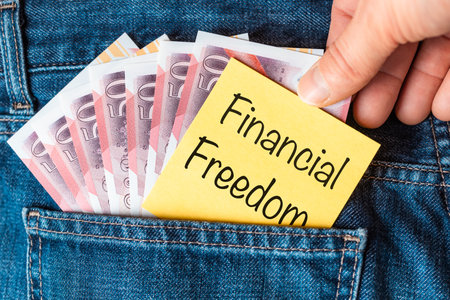 The concept of financial freedom in the United Kingdom. UK money in the pocket of trousers, hand putting a piece of paper with the words "Financial Freedom" into the trousers. Close upの写真素材