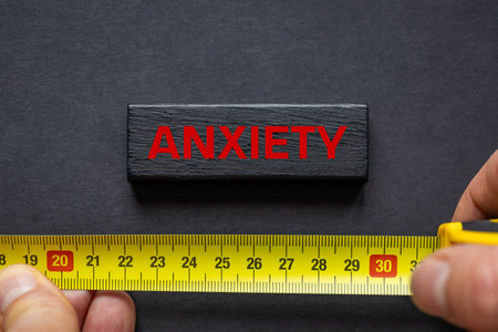 Anxiety. Red lettering on a black block and black background. A measuring tape indicates a growing...