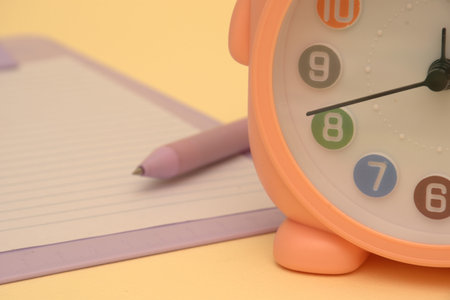 Close up of alarm clock with notebook and pen on yellow background.のeditorial素材