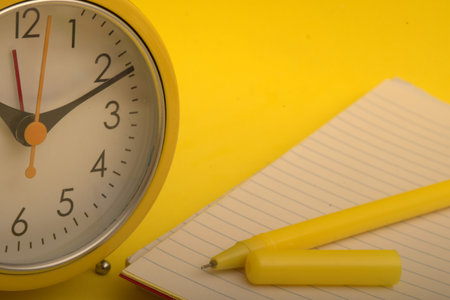 Yellow alarm clock, notebook and pen on a yellow background. time concept