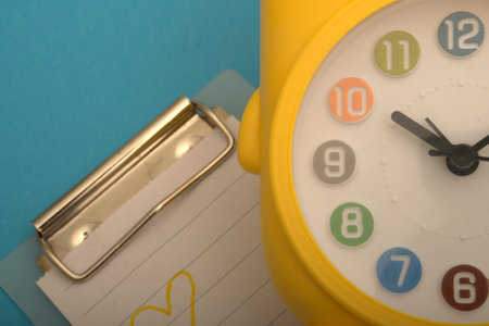 Yellow alarm clock and paper clip on blue background. Time concept.のeditorial素材