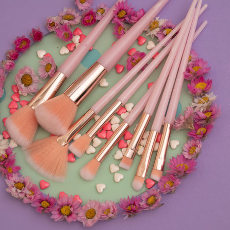 makeup brushes and pink flowers on a purple background. top viewの写真素材